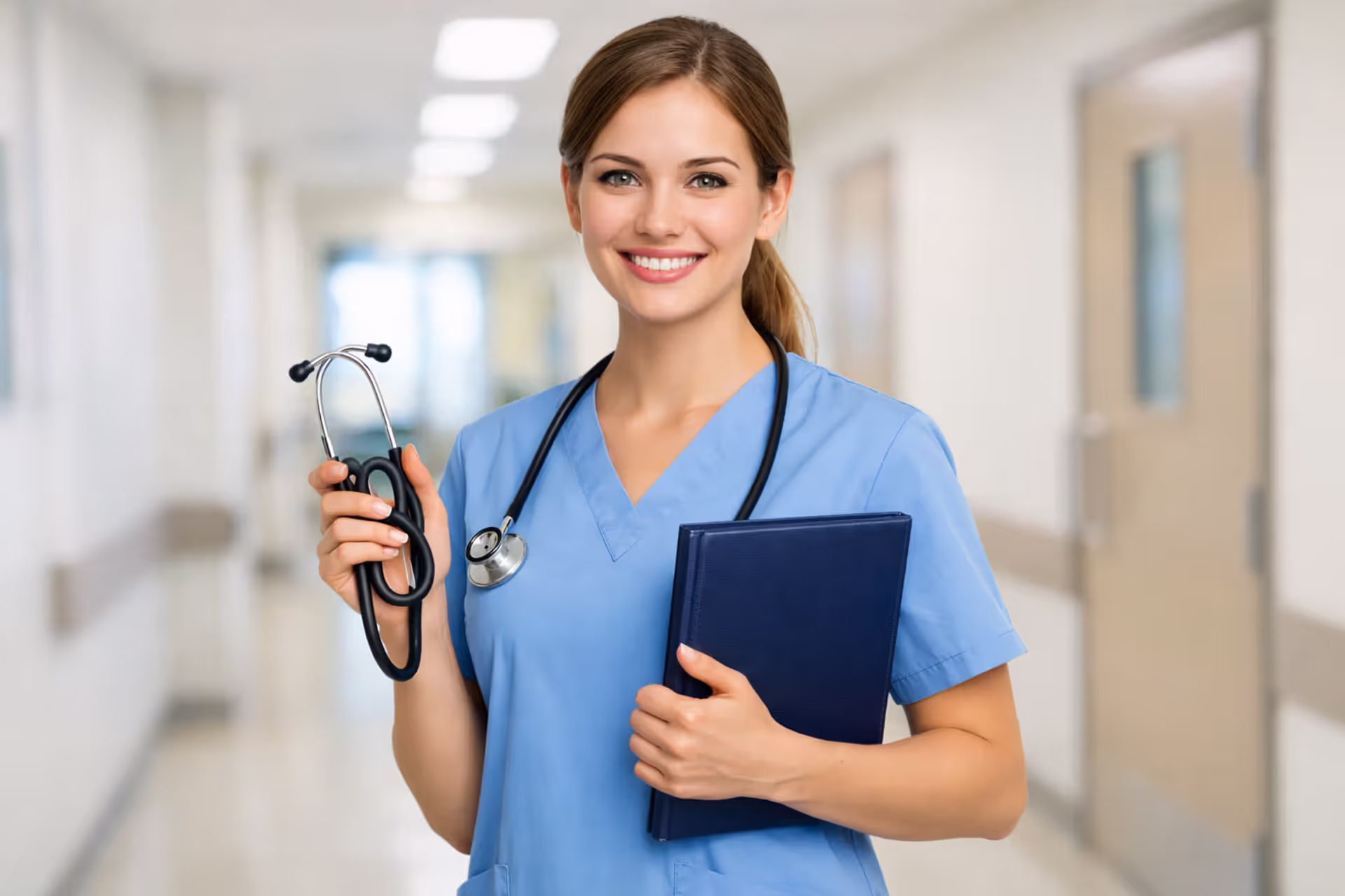 Young smiling nurse in blue scrubs holding a stethoscope and graduation diploma in a bright hospital hallway